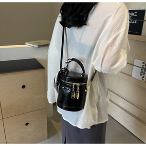 Detail of black cylindrical bucket bag with silk scarf handle and golden lock zippers