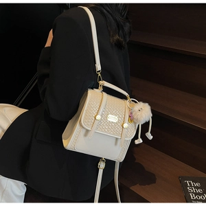 Dettaglio della patta in pelle intrecciata beige e ciondolo in peluche sullo zaino versatile