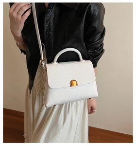 Sac à main blanc motif lychee avec fermoir doré porté par un mannequin en tenue chic