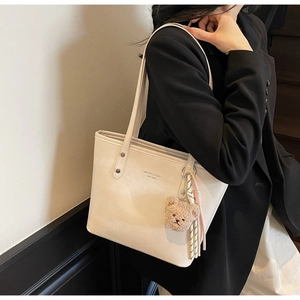 Detail of cream tote bag with bear charm and scarf accessory on black blazer