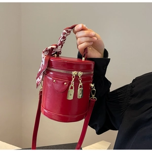 Detail of red patent bucket bag featuring a decorative silk scarf on the handle