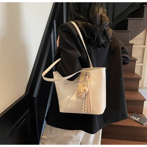 Detail of cream leather tote bag with brand logo and cute plush bear accessory charm