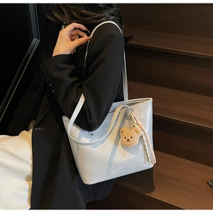 Detail of silver tote bag featuring cute plush bear charm and woven rope decoration