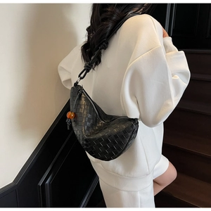Detail of black woven crescent bag featuring a stylish orange spherical charm