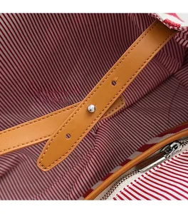 Détail de la doublure rayée rouge et bandoulière en cuir marron avec boucle en métal argenté