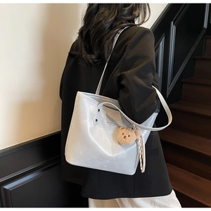 Detail of silver tote bag with plush bear charm worn on shoulder over a stylish outfit