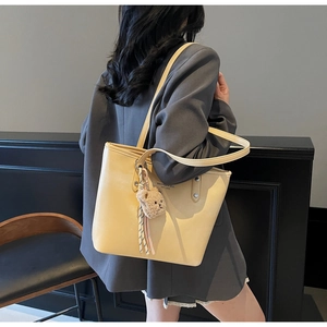 Detail of cream leather tote bag featuring a brand logo and a plush bear pendant charm
