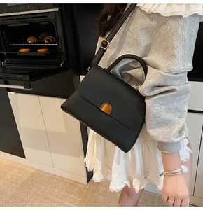 Détail d'un sac à main noir en cuir litchi avec poignée incurvée et bouton pression doré