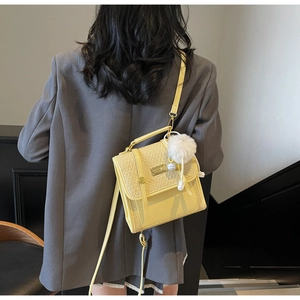 Dettaglio della borsa a tracolla in pelle giallo chiaro con trama intrecciata e pompon
