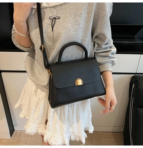 Détail du sac à main en cuir grainé noir avec boucle dorée porté par un mannequin