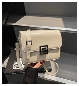 Detail of cream flap square bag with glossy finish and geometric metal buckle on black book