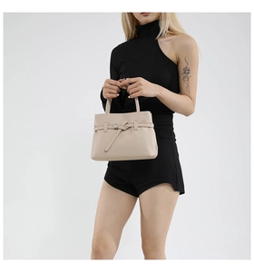 Close-up of beige lychee grain leather handbag featuring silver ring buckle and knot detail