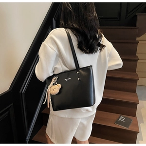 Detail of black leather tote bag with plush bear charm and white branded lettering