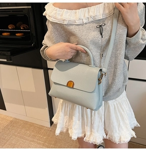 Detail of light blue lychee pattern leather handbag with golden metal buckle and top handle