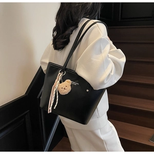 Detail of black tote bag featuring plush bear and tassel charms on a stylish PU leather surface