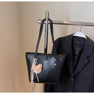 Detail of black PU leather tote bag with white branding text and cute plush bear charm