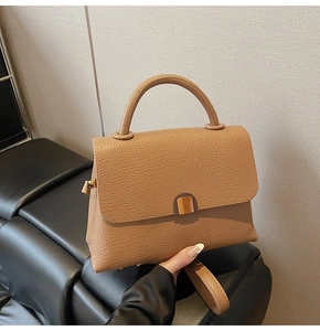 Detail of camel lychee grain leather handbag with round metal clasp and flap closure