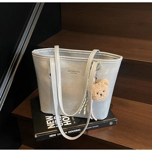 Detailed shot of silver tote bag with plush bear charm on dark wooden steps