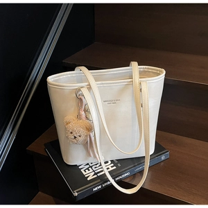 Close-up of white tote bag with brown plush bear charm on wooden stairs with books