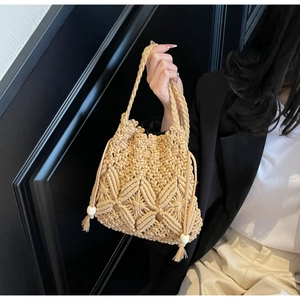 Detailed close-up of woven straw bucket bag with intricate crochet patterns and wood bead tassel