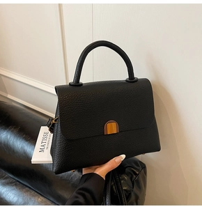 Detail of black lychee grain leather handbag featuring a half-round bronze metal clasp