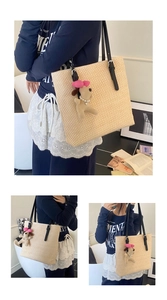 Detail of hand-woven straw tote bag featuring black faux leather straps and a dog charm