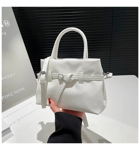 Close-up of white pebble leather handbag with gold metal buckle and hand strap detail