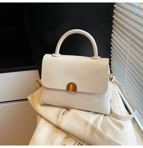 Close-up of minimalist cream pebbled leather handbag with golden hardware on white blazer