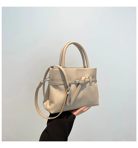 Detail of off-white lychee grain leather tote bag with dual handles and metal buckle accent
