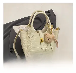 Detailansicht der beigefarbenen Krokodil-Handtasche mit goldener Schließe und Teddy-Anhänger
