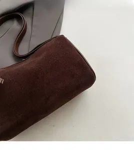 Close-up detail of soft brown suede texture and leather strap stitching on small square bag