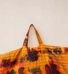 Detail of a large camouflage tote with reinforced fabric handles and abstract orange pattern