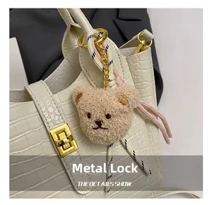 Detailansicht der weißen Krokodilleder-Tasche mit Goldverschluss und Plüschbär-Anhänger