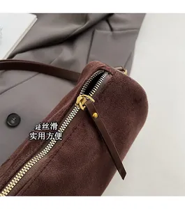 Detail of the smooth metal zipper and brown suede material on the cylindrical crossbody bag