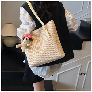 Detail of hand-woven straw tote bag featuring yellow leather strap and plush dog charm
