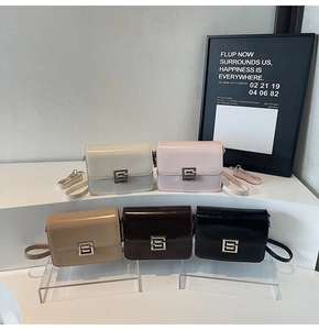 Five assorted glossy crossbody square bags with silver metal buckles on white display stand