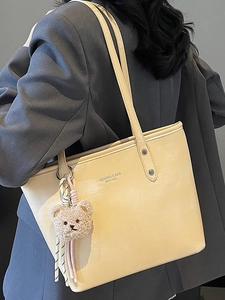Large beige leather tote bag with brand lettering and a cute bear charm for women