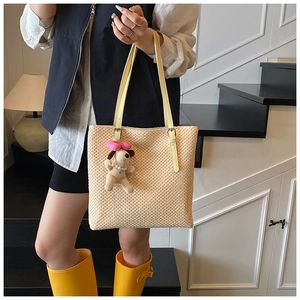 Detail of handwoven straw tote bag featuring yellow leather strap and a cute puppy charm