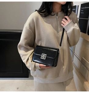 Detail view of the silver square metal twist lock on a black glossy leather crossbody bag