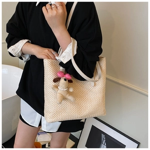 Detail of handwoven beige tote bag with white leather strap and plush dog charm