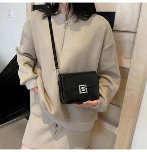 Close-up of black glossy leather small square bag with silver clasp on female model
