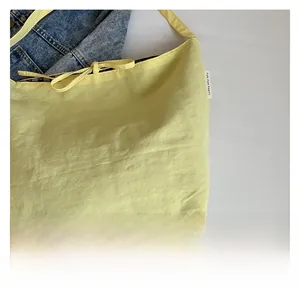 Detail view of light yellow nylon tote bag featuring side brand label and pattern lining