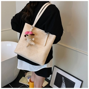 Detail of a beige woven straw tote bag with white leather straps and a cute dog charm