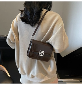 Detail of a dark brown patent leather crossbody bag with silver geometric metal clasp