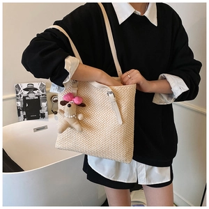 Detail of hand-woven straw tote bag with cream leather strap and pink puppy charm accessory