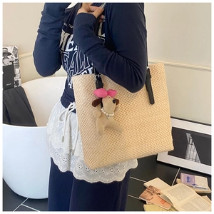 Detail of a beige straw tote bag with black leather straps and a cute plush dog charm