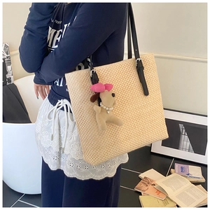 Straw tote bag detail with cute plush puppy charm and black leather shoulder strap