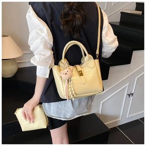 Detail der beigen Beuteltasche mit Krokodilmuster, Bärenanhänger und passender Clutch-Tasche