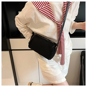 Detailed side view of a black cylinder crossbody bag with golden hardware on a model