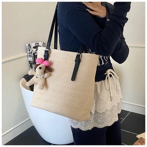 Detail of hand-woven straw tote bag with black adjustable straps and cute puppy charm